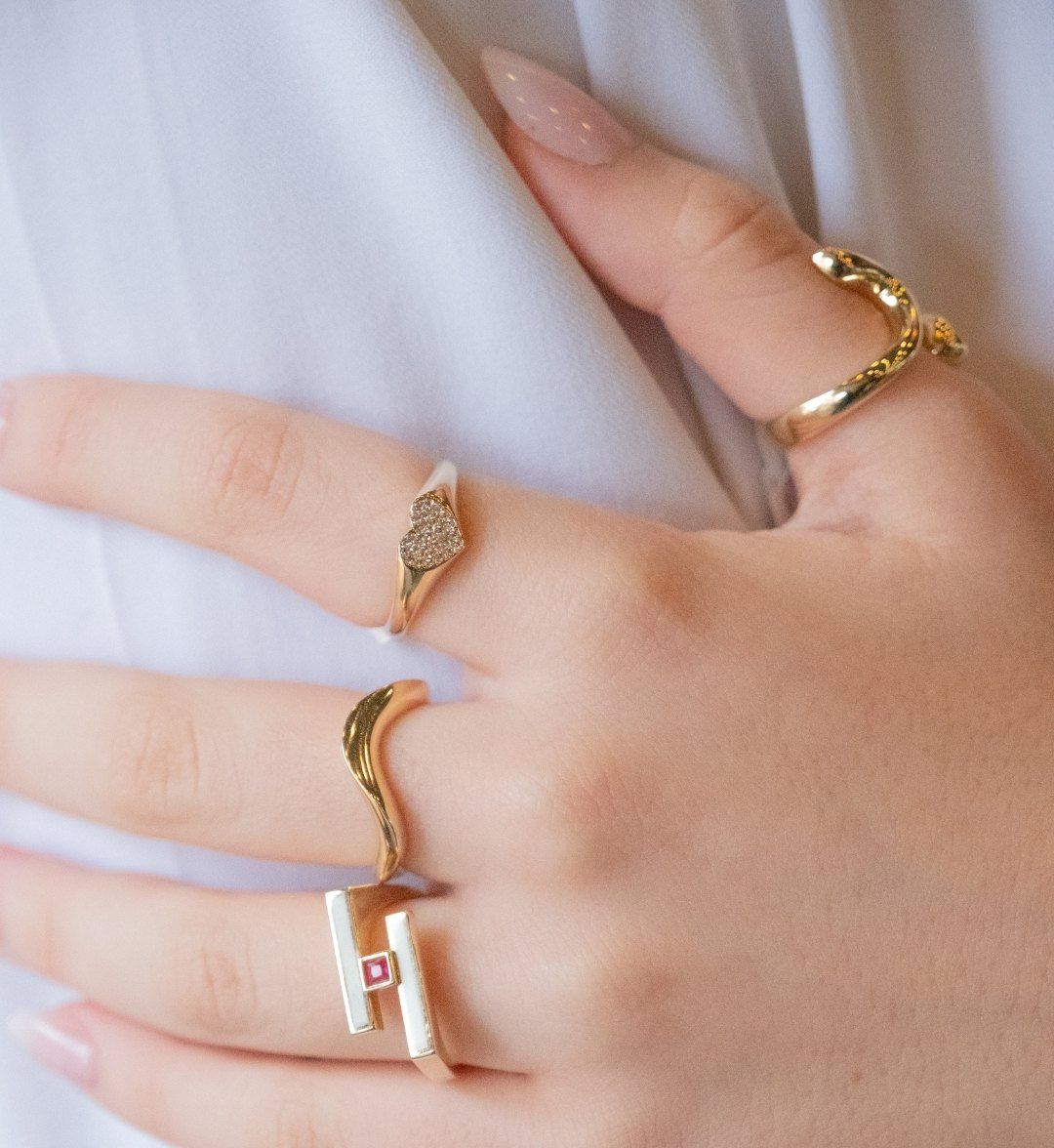 Four modern designer gold rings on one hand: heart pavé, wavy, twisted and pink-stone