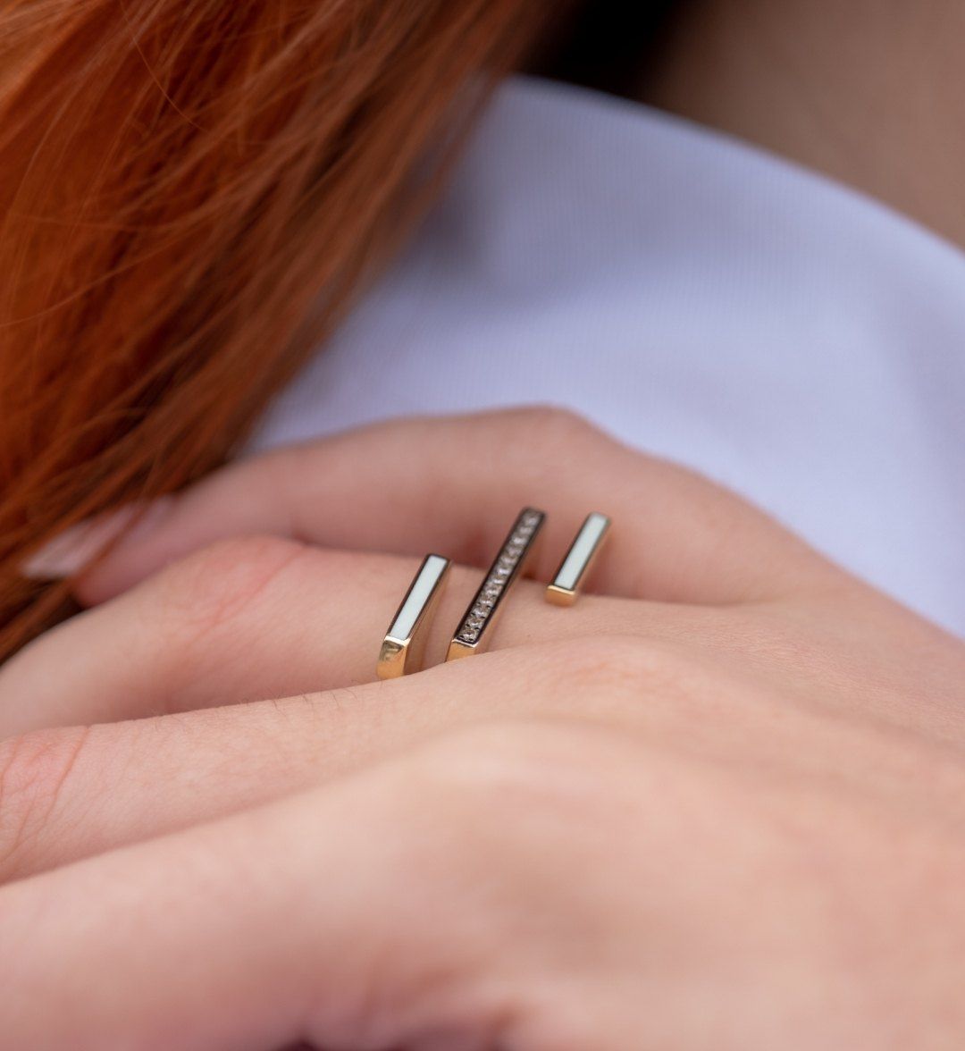 Open modern gold ring with three bars, the middle one stone-set, close-up on the finger