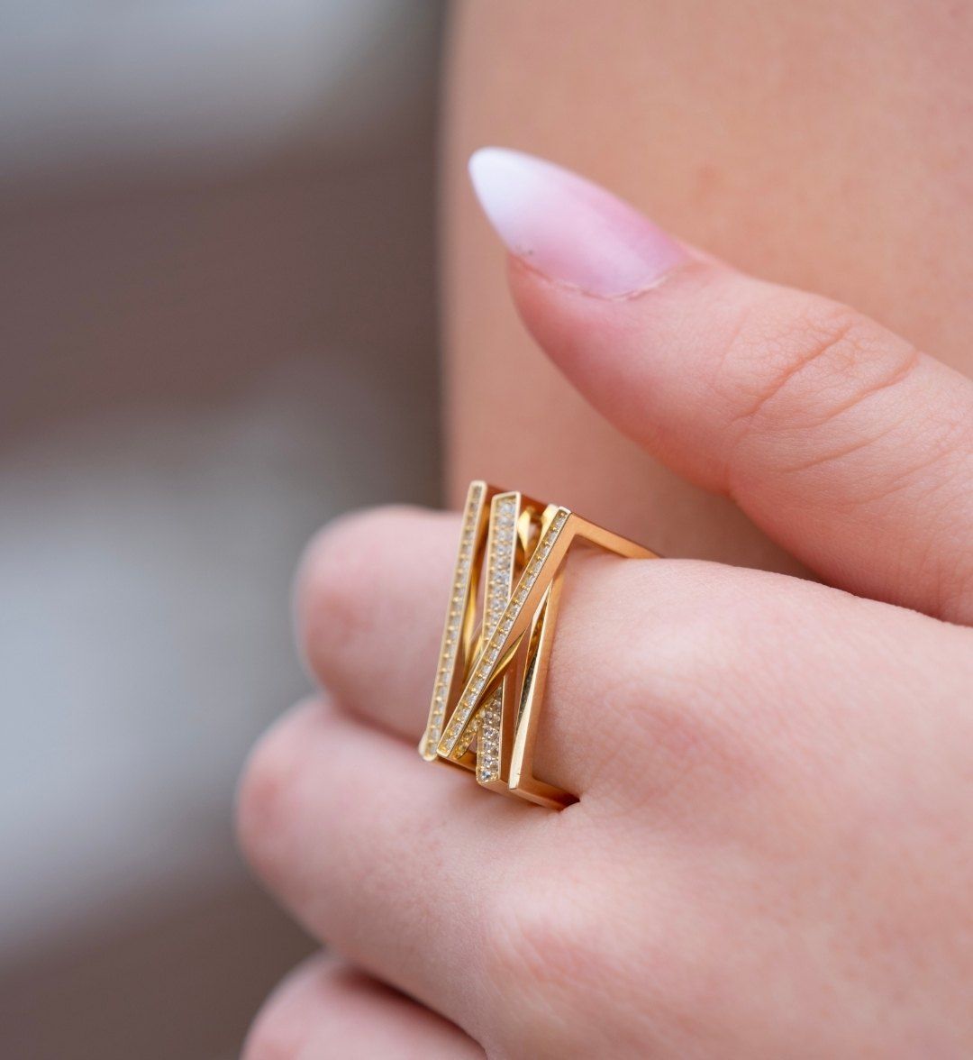 Wide modern designer gold ring of crossing stone-set bands worn on the finger