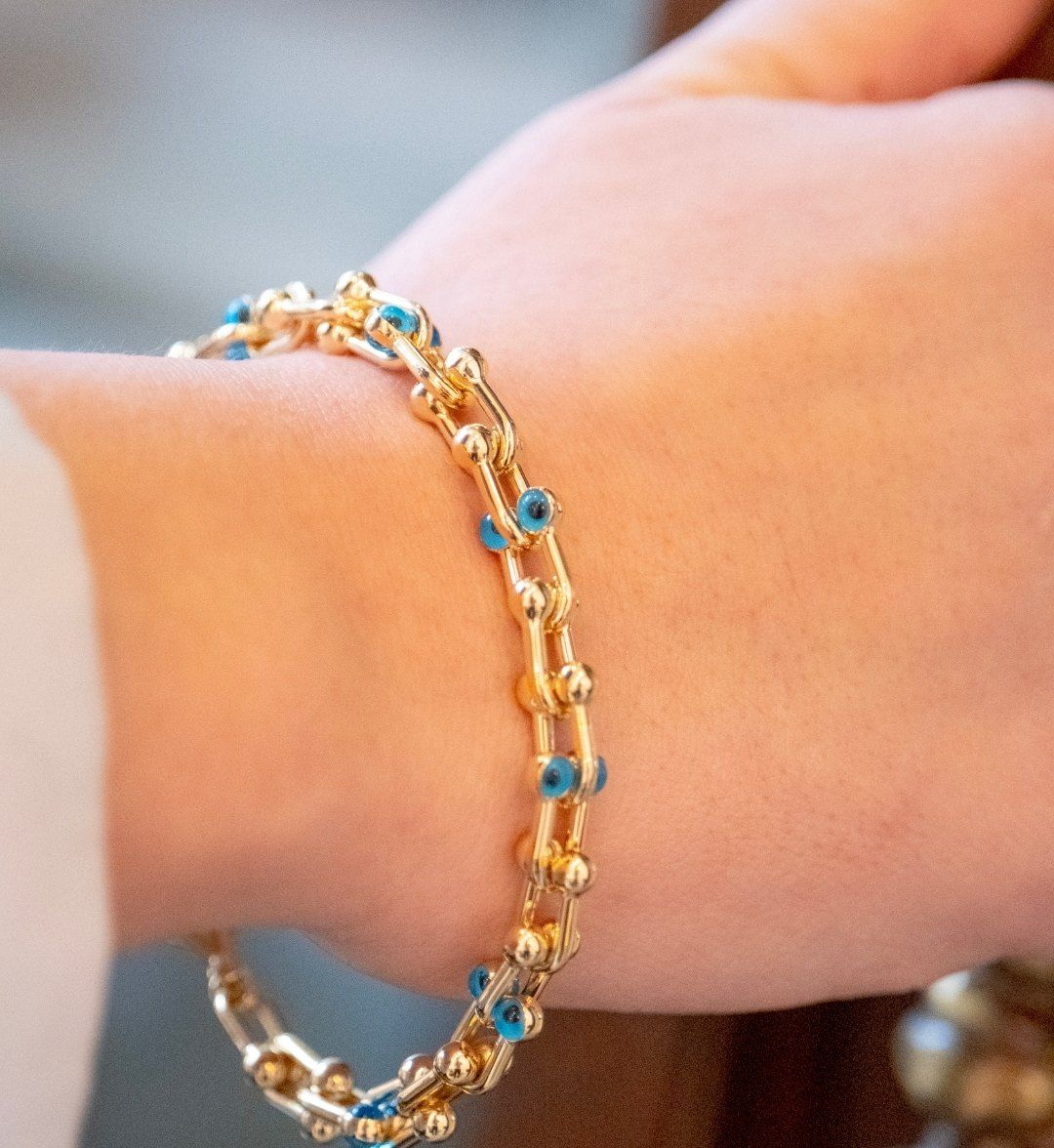Gold chain bracelet with U-shaped links set with small blue beads on a model's wrist