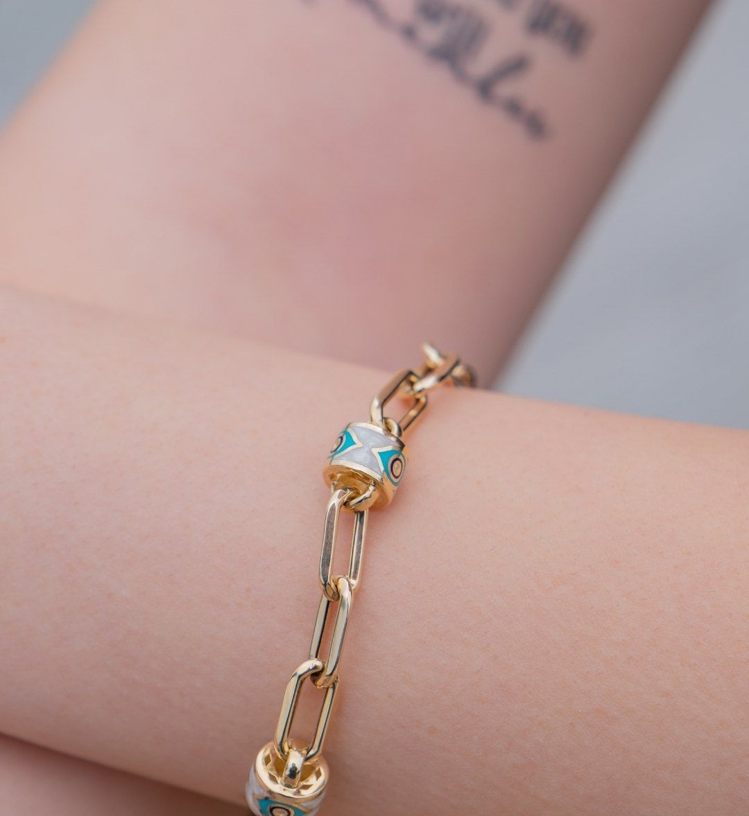 White and turquoise patterned bead on a long-link gold bracelet, close-up on the arm