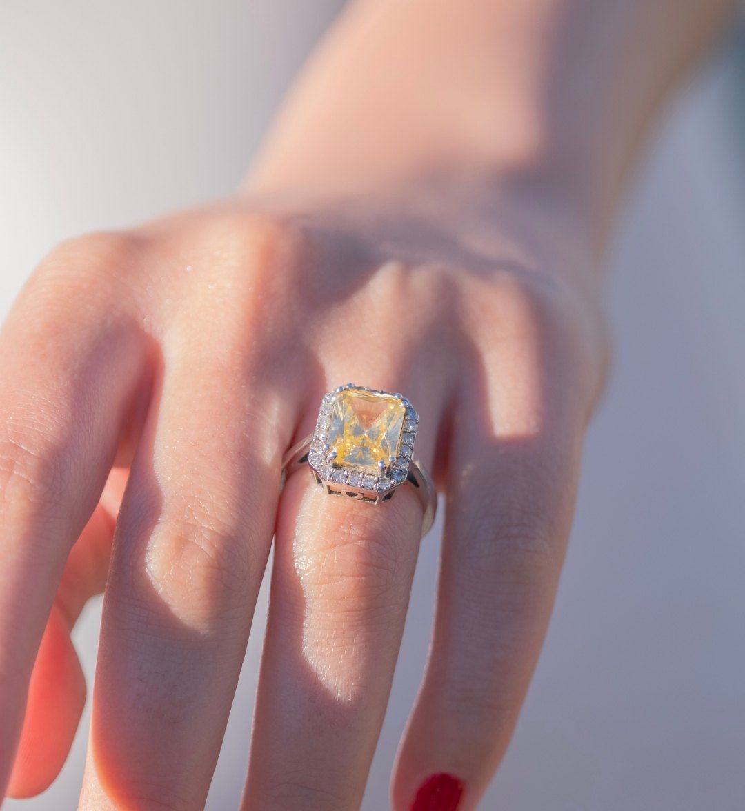 Silver-toned ring with a rectangular yellow stone framed by white stones on the finger