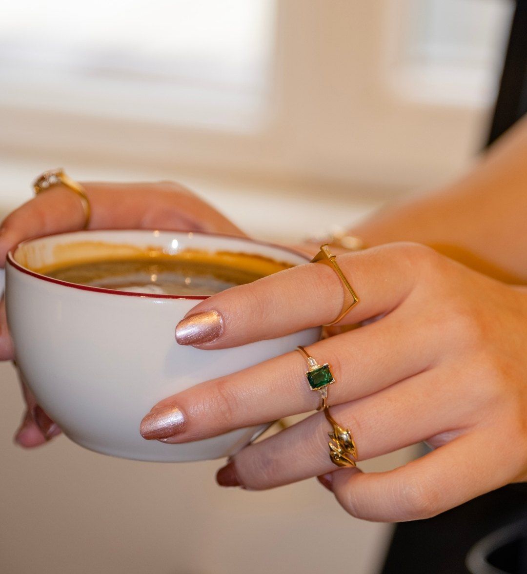 Green stone ring worn with other gold rings on hands holding a coffee cup