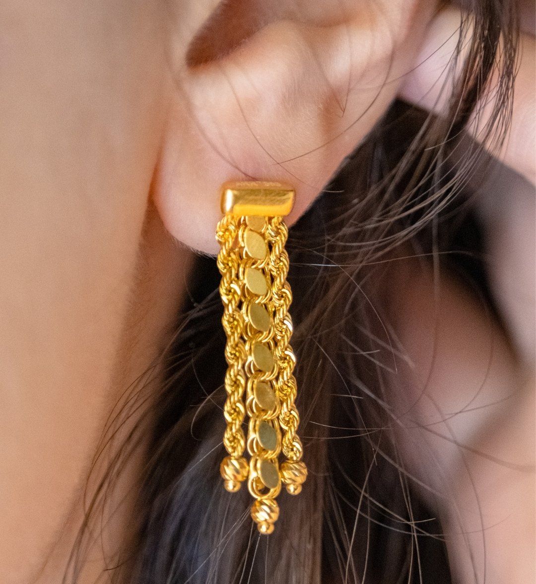 Gold tassel earring of twisted rope chains and discs worn on the ear, close-up