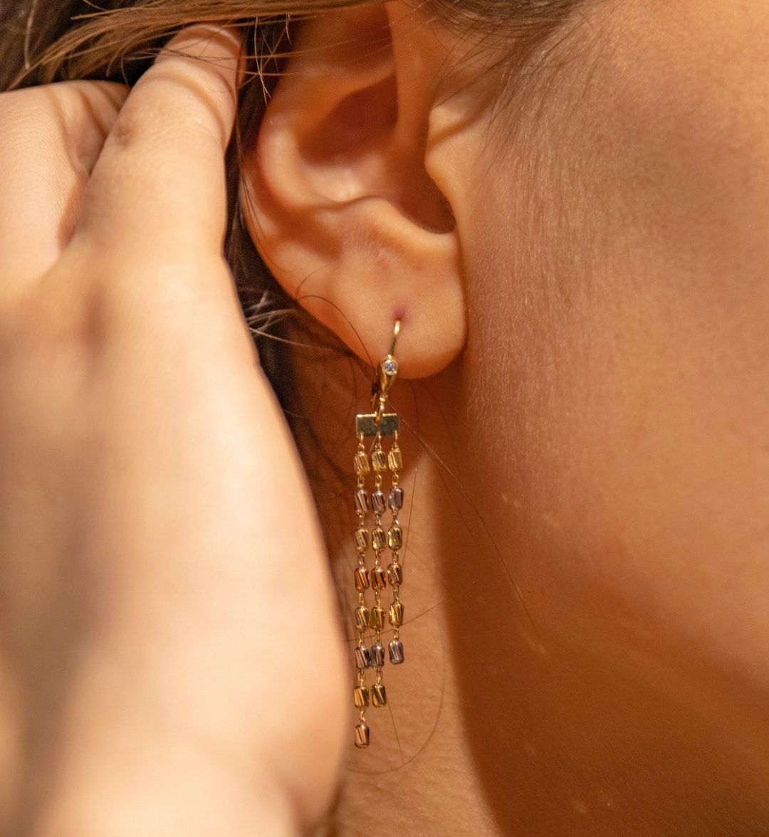 Gold tassel earring with fine tri-colour chains hanging from a stone-set hook on the ear
