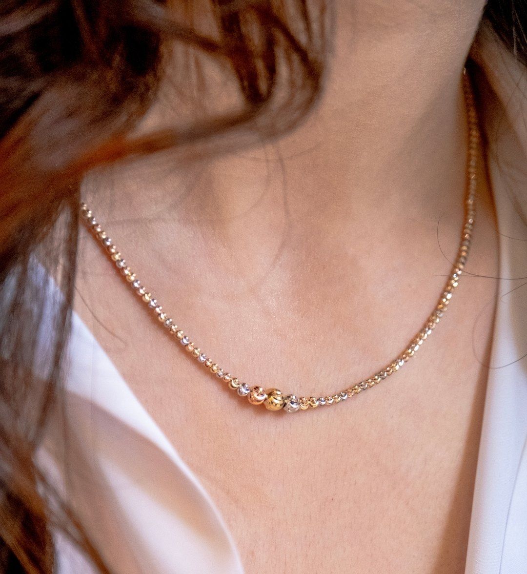 Fine two-tone beaded necklace with gold balls at the centre, worn close to the neck