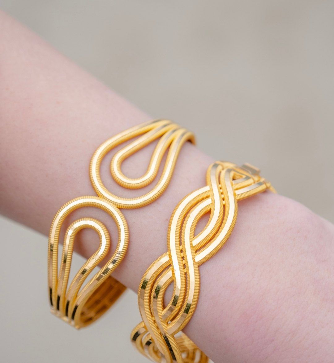 Two designer gold cuffs on the wrist: a teardrop-loop design and a braided design