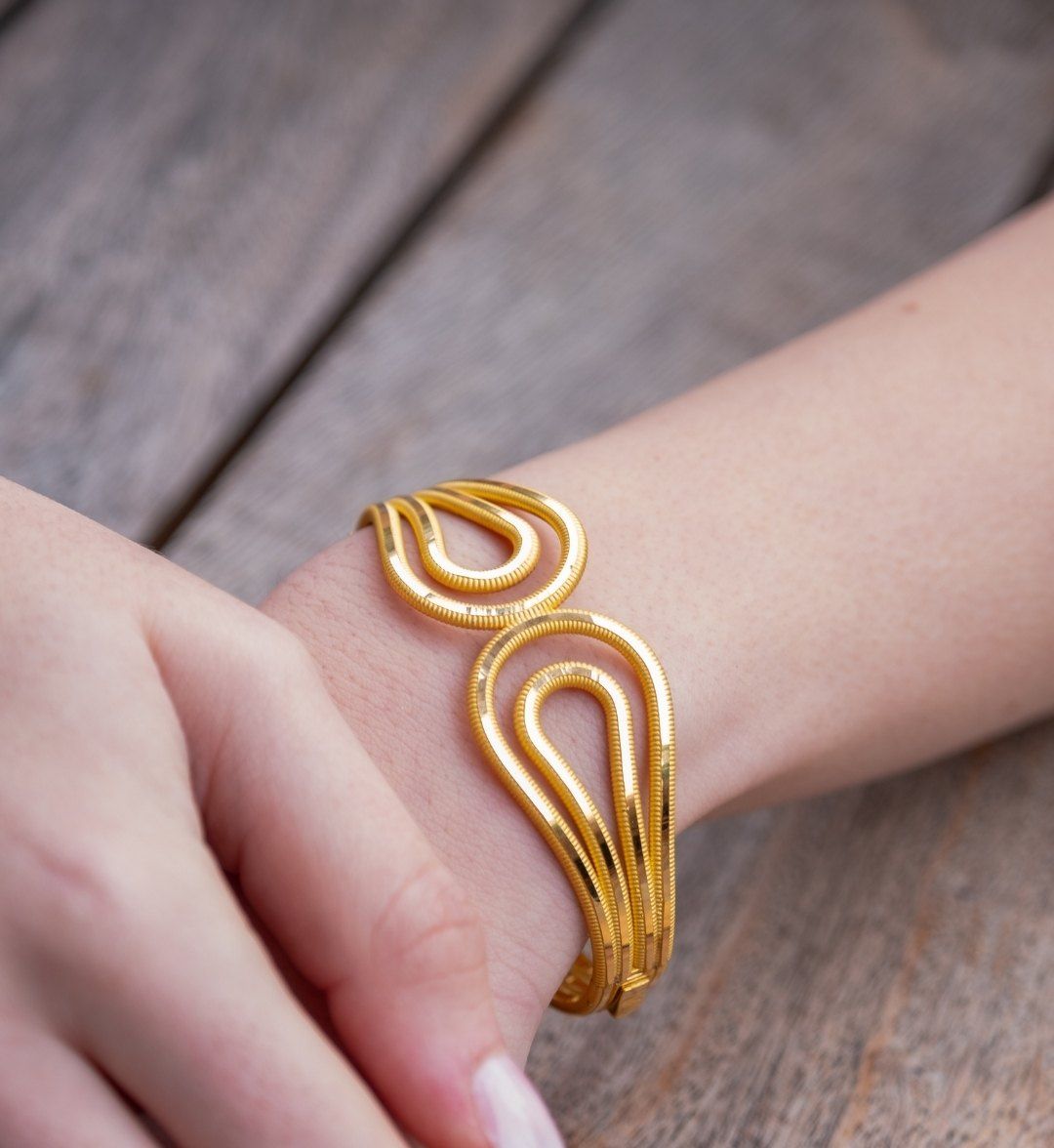 Designer gold cuff of fine wires in teardrop loops on a wrist resting on wood