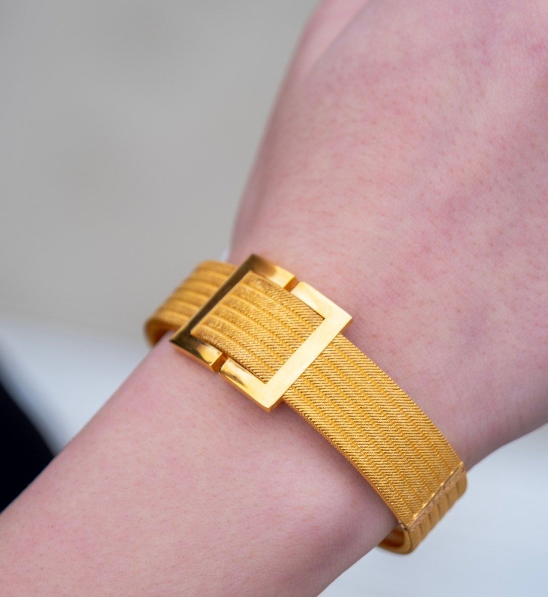 Belt-buckle designer gold cuff with a fine ribbed texture worn on the wrist