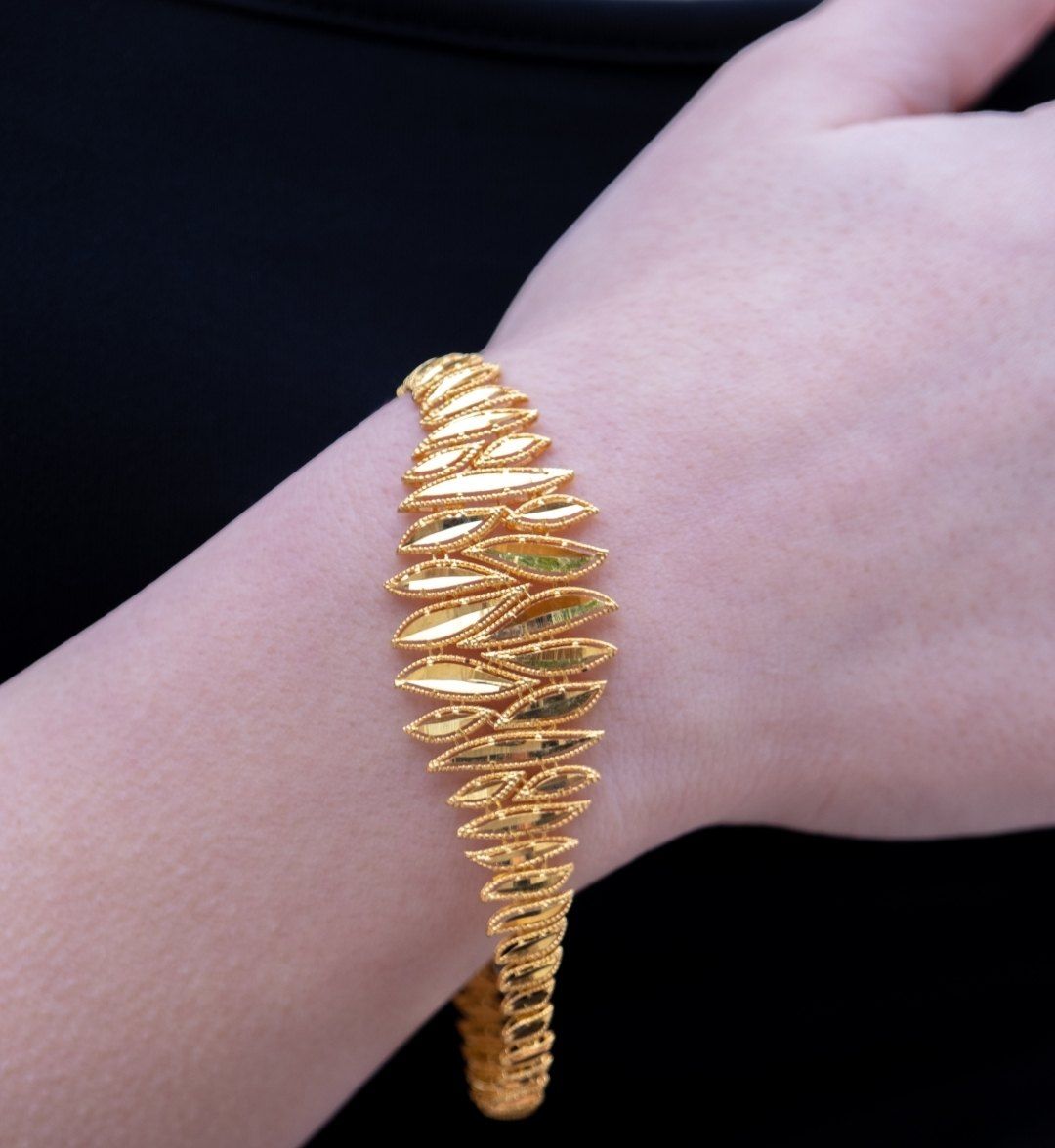 Yellow gold designer bracelet of overlapping pointed leaves on the wrist, black backdrop