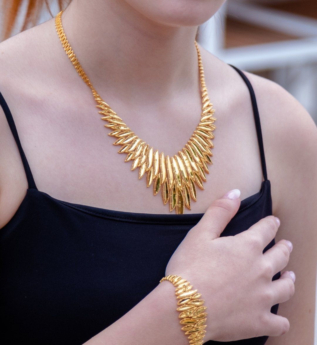 Gold leaf collar with a matching leaf bracelet on the wrist, worn with a black strappy dress