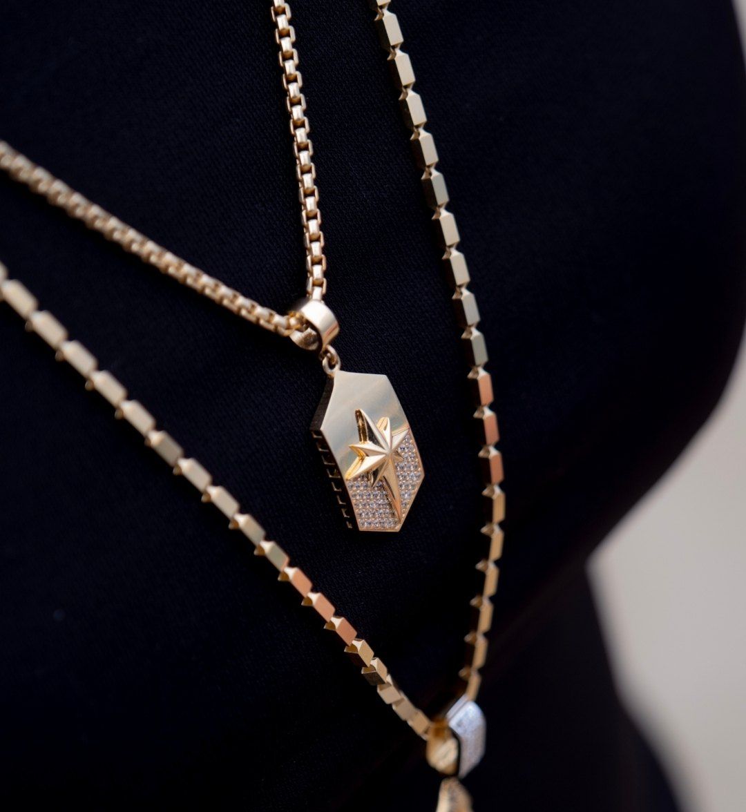 Star plate pendant layered with a second long-link gold necklace over black clothing