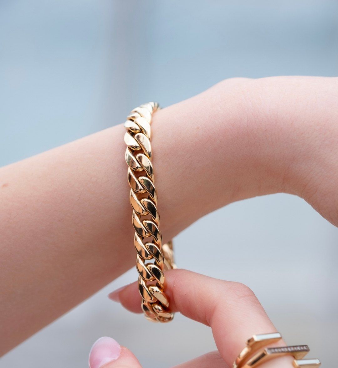 Chunky polished curb-link gold chain bracelet held between the fingers, close-up