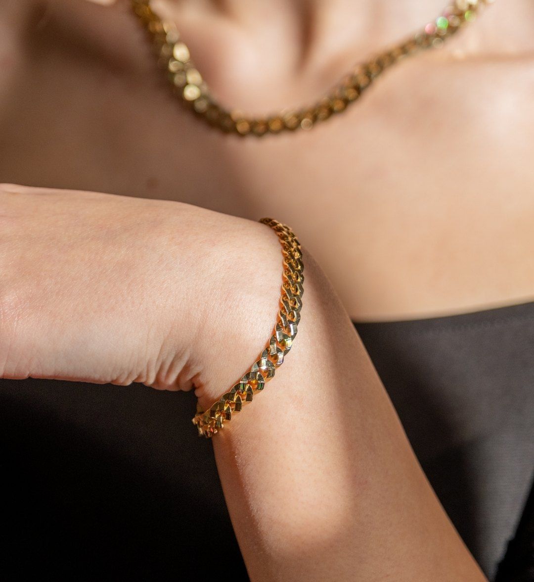 Flat curb-link gold bracelet on a model's wrist, with a matching chain necklace behind