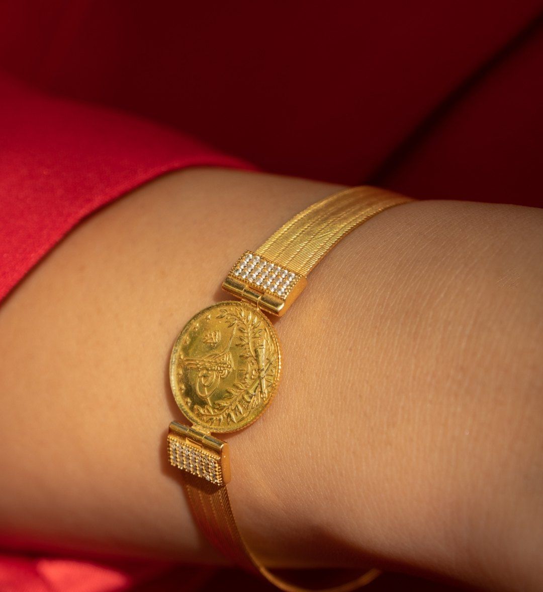 Gold coin bracelet with a tughra coin and white stone-set links on a mesh band, on the wrist