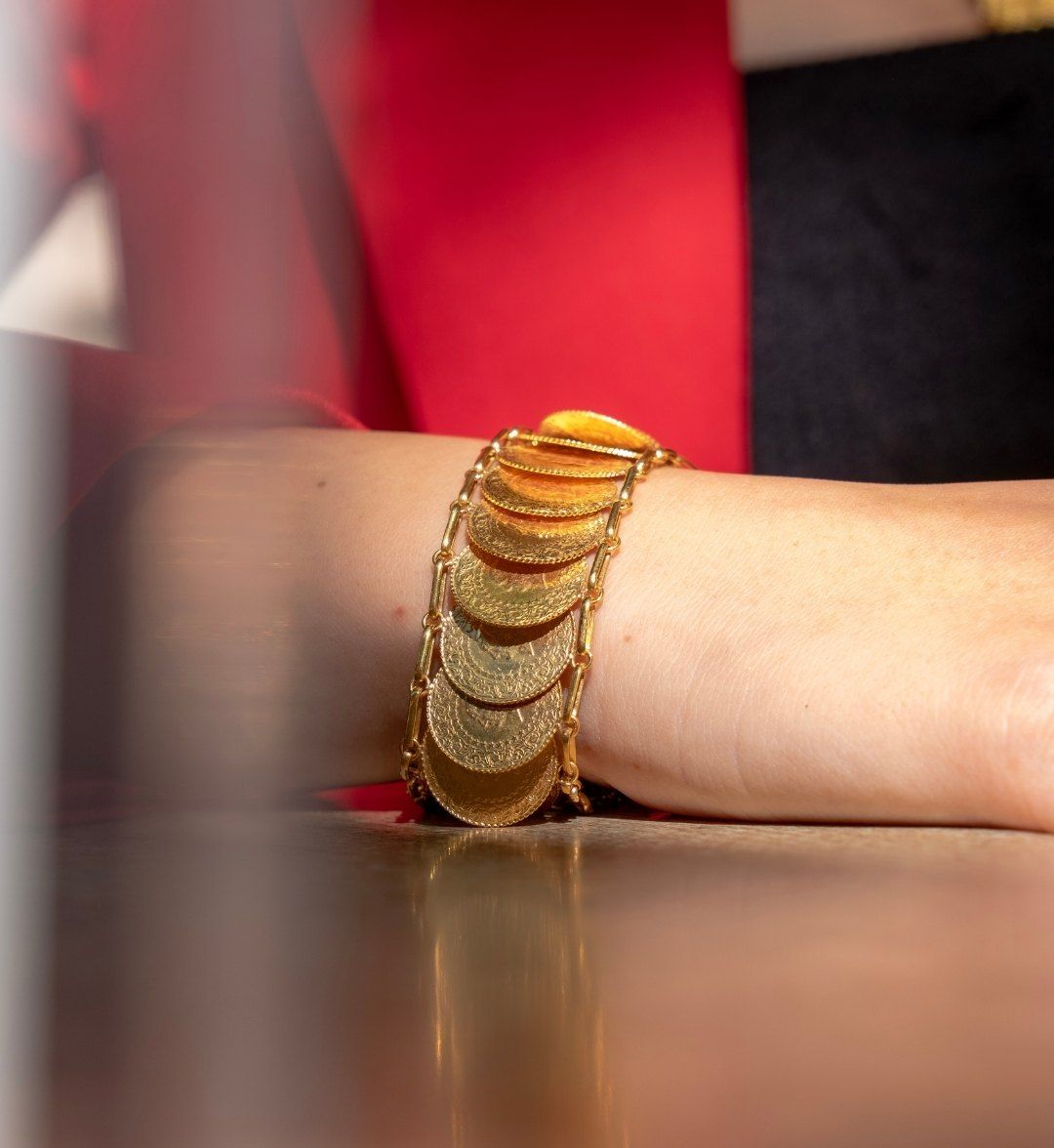 Wide bracelet of overlapping gold coins on a wrist resting on a table, side view